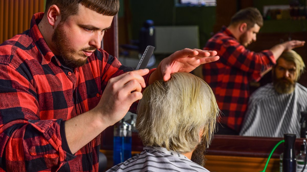 A barber styling a client's hair with a comb in a traditional barbershop