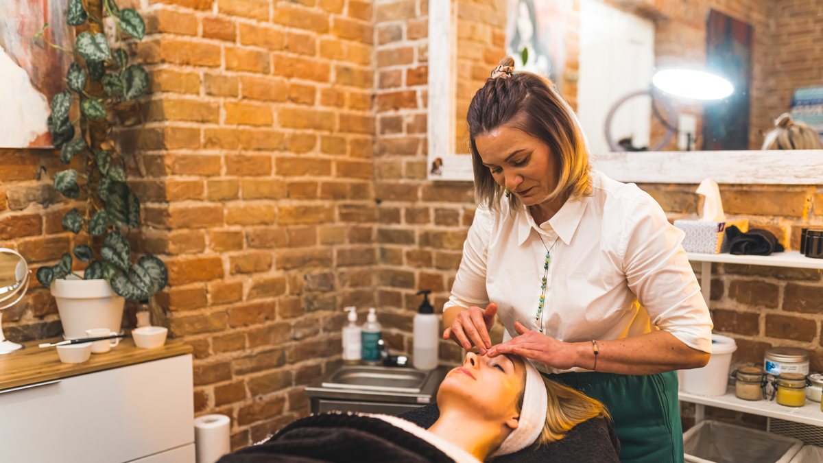 A beautician giving a client a facial massage in a brick-walled beauty salon