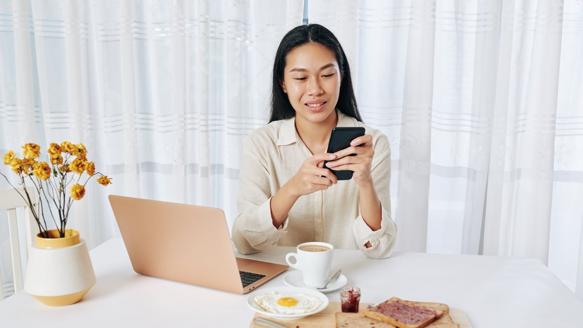 A woman checking her phone over breakfast and coffee at home
