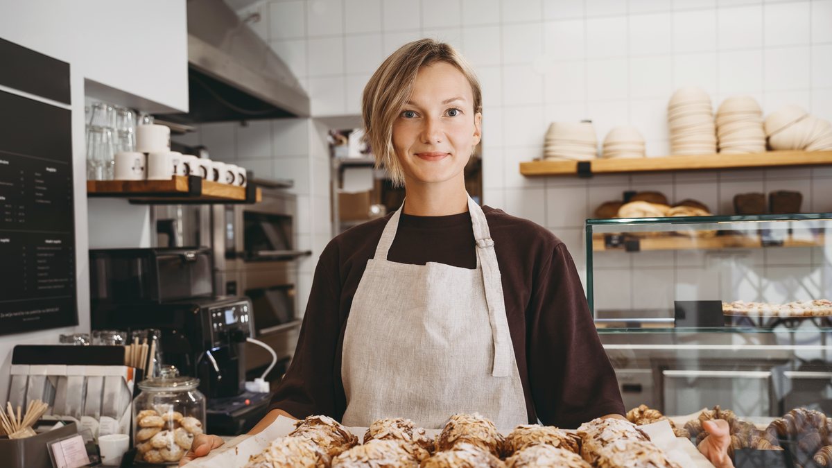 A smiling baker holding a tray of freshly baked croissants behind the bakery counter