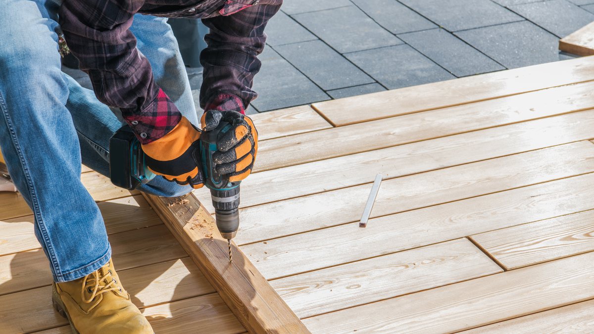 A tradesman screwing down new timber deck boards with a cordless drill
