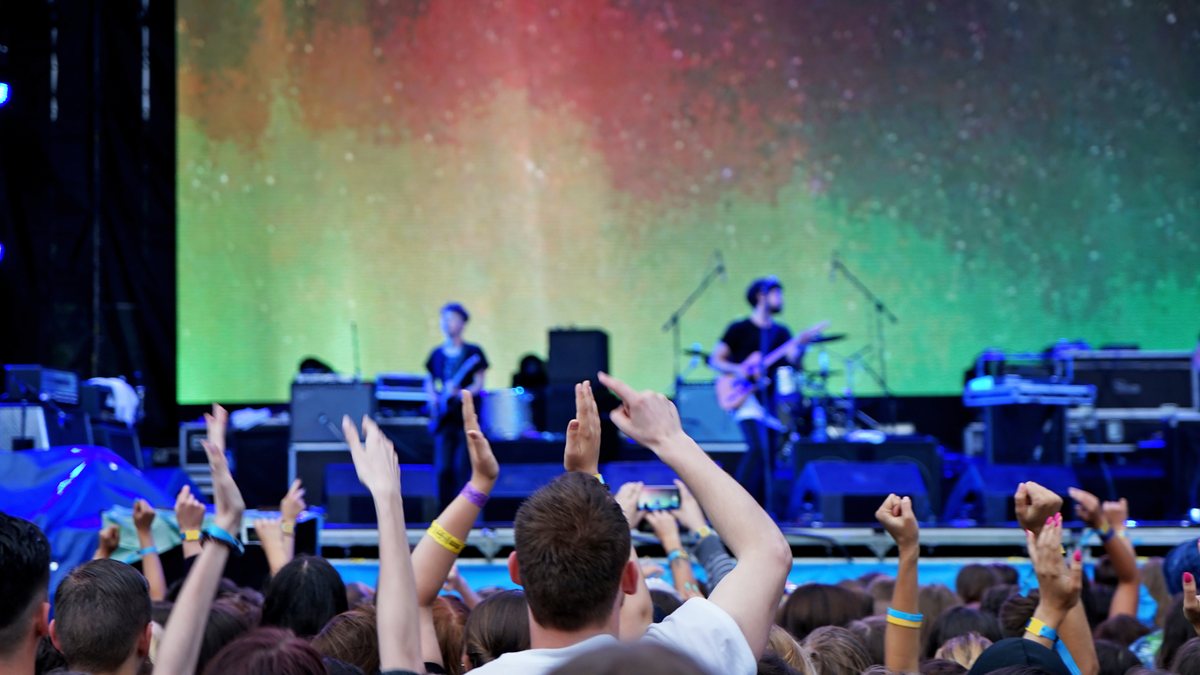 A crowd with hands in the air in front of a band on an outdoor stage