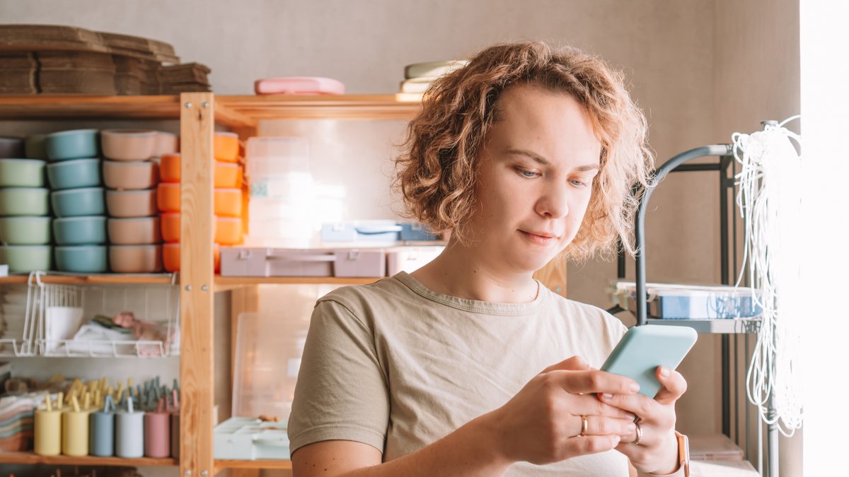 A small shop owner checking her phone among shelves of stock in her store