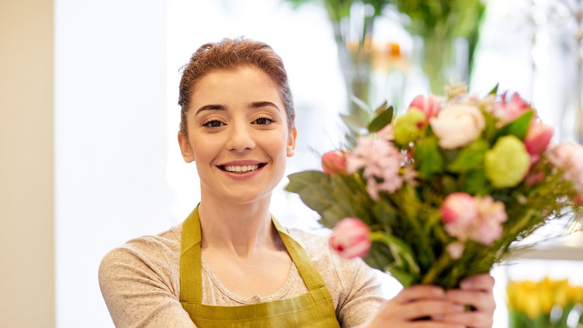 A smiling florist holding up a fresh bouquet in her flower shop