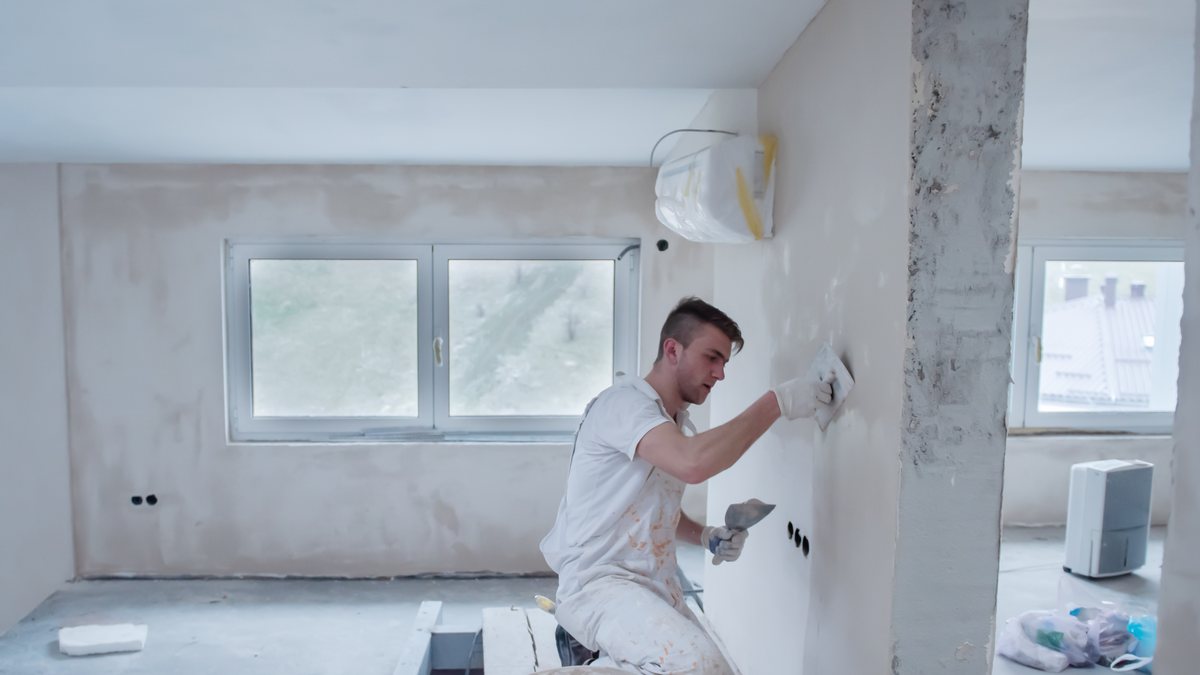 A tradesman plastering the walls of a room under renovation