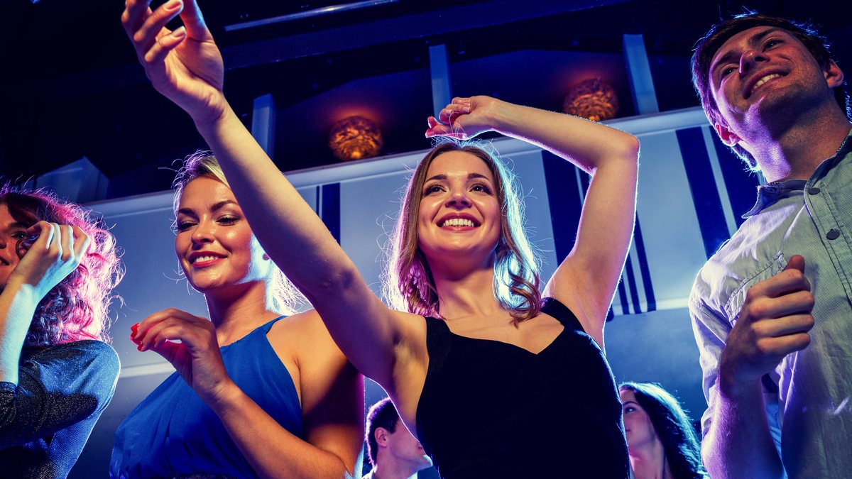Friends dancing and smiling under the lights at a club night