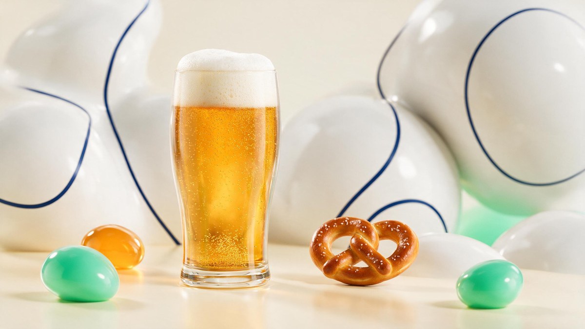 A soft-3D pint of golden beer with a frothy head beside a pretzel on a warm cream surface