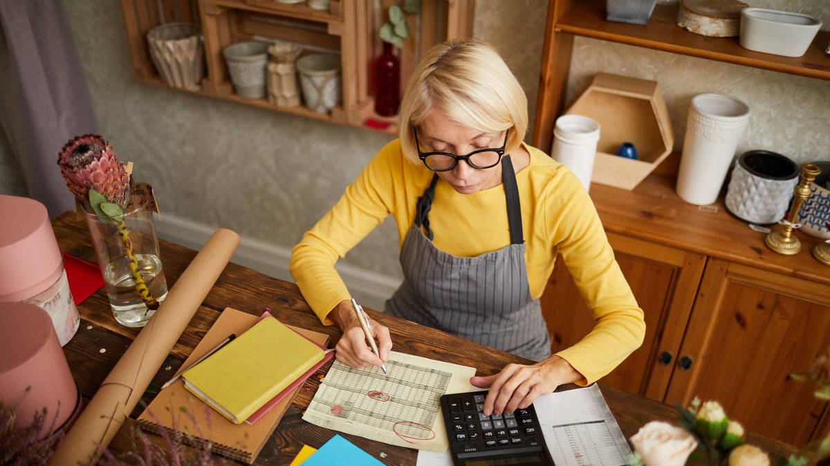 A small shop owner working out her costs with a calculator and paperwork