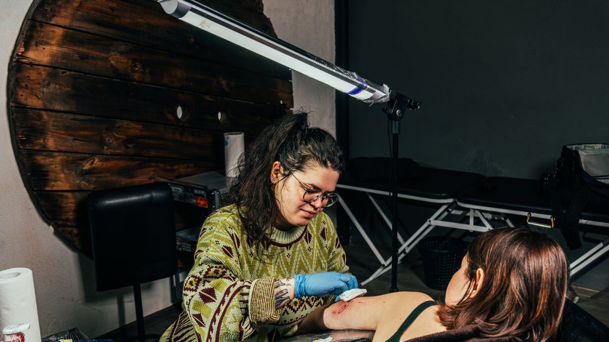 A tattoo artist in gloves tattooing a client's arm in her studio